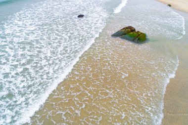 Kumlu bir plajda yaklaşan ve dalgaları kıran doğal kaya dokusunun hava perspektifi