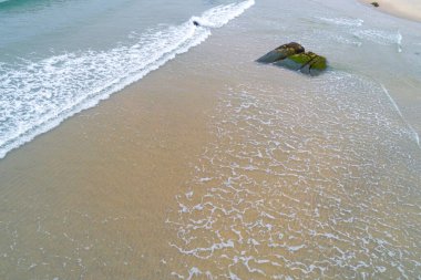 İlginç kaya oluşumu ve okyanus dalgalarıyla sakin bir sahil kenarı manzarası.