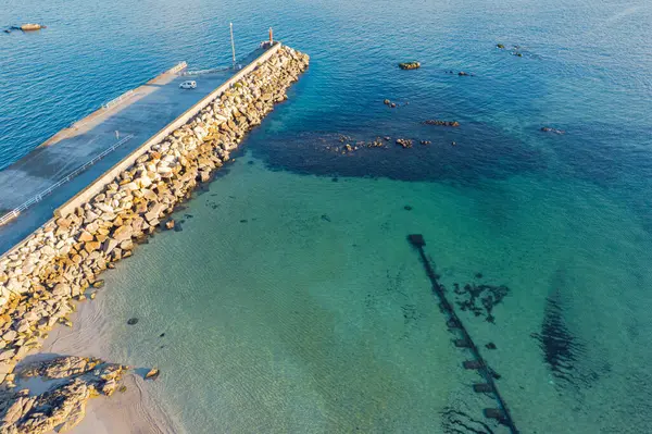 Gün batımında berrak okyanus suyuna uzanan bir iskelenin havadan görünüşü, denizcilik yaz arkaplanı kavramı