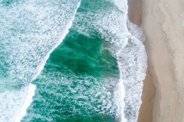 Geniş kıyı manzarası canlı yeşil dalgalar güneş ışığıyla aydınlanan sahile çarpıyor. Bir İHA 'nın havadan görüntüsü.