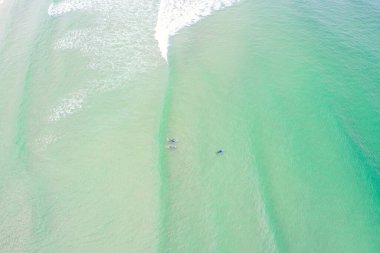 İnsansız hava aracı fotoğrafçılığı. Üç sörfçü sahilde dalga kırmayı bekliyor.