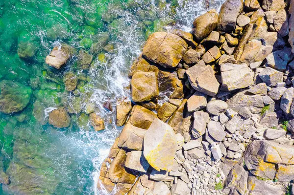 Kayalık bir sahil kıyısı ve dalgalı okyanus suyunun tepeden aşağı insansız hava aracı görüntüsü