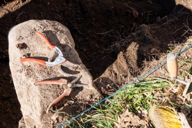 Kazılmış topraklı büyük bir kayanın üzerinde bahçe aletleri.