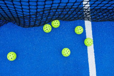 Canlı Pickleball Sahnesi Mavi Mahkeme Dağılmış Yeşil Toplar ve Net Oynamaya Hazır.