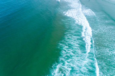 Geniş turkuaz bir okyanusun havadan görünüşü. Uzun, dalgalı ve kumsalda yaşayanlar.