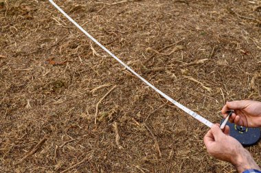 Bir Arazi Çizelgesini Ölçmek için Ölçüm Bantını Kullanan Araştırmacı