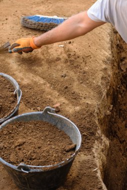 Bir arkeolog bir malayla kazı alanında kazı yapıyor. Geçmişi ortaya çıkarmanın titiz çalışmalarını kabul et..