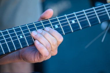 Bir müzisyenin eli gitar ensesinde akor çalıyor, müzik alıştırması konsepti.