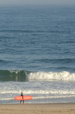 Kırmızı sörf tahtası olan bir sörfçü sörf yapmak için denize açılıyor.