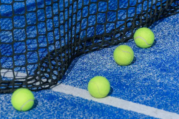 Mavi bir kortta ağın yanında dört padel top. Bir Padel Mahkemesi Detayı