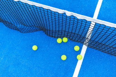 Mavi bir kortta ağa saçılmış bir grup sarı padel topu. Bir Padel Mahkemesi Detayı