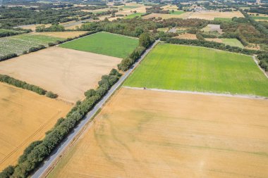 Toplanan buğday tarlaları ve yukarıdan toplanan yeşil ekinlerle kırsal alan.