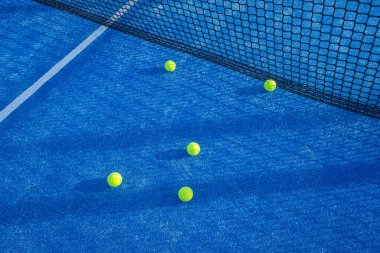Sarı padel topları kalenin yanındaki mavi korta saçılmış..