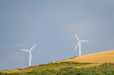 Yeşil bir tepede iki rüzgar türbini temiz yenilenebilir enerji sürdürülebilirliği kavramı üretiyor