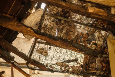 Yanmış ve tahrip olmuş bir tavandan yatak yaylarına bakıyorum..