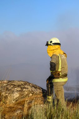 Yalnız bir itfaiyeci Dumanlı bir arka plana karşı bir tepede duruyor