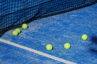 Açık mavi bir padel kortunda sarı toplarla antrenman yapmak için spor aletleri.