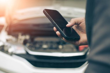 İşadamı yolda arızalı bir arabaya bakarken cep telefonu kullanıyor..