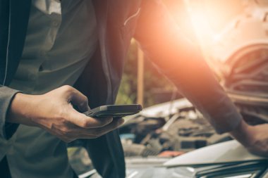 İşadamı yolda arızalı bir arabaya bakarken cep telefonu kullanıyor..