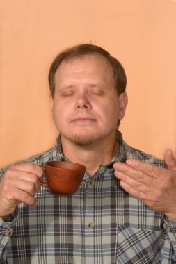 Ekose gömlekli genç bir adam turuncu arka planda kahve kokusunu içine çekiyor.