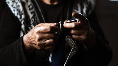 Yaşlı bir kadının elleri kancayla örgü örüyor. Büyükanne beyaz örgü örüyor. El işi konsepti