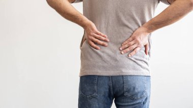 Sırt ağrısı. Kas ağrısı çeken ve açık gri arka planda zorlanan genç bir adam..