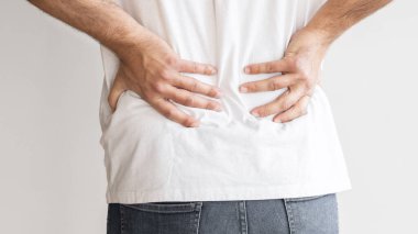 Sırt ağrısı. Kas ağrısı çeken ve açık gri arka planda zorlanan genç bir adam..