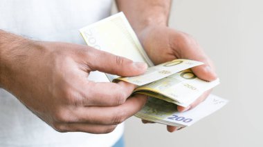 Avro banknotları teklif eden ve elinde avroluk para tutan bir adam. Euro, dolar banknotları, Avrupa Birliği kağıt para birimi. Para biriktirme kavramı.