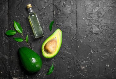 Taze avokado ve bir şişe. Rustik siyah arka plan üzerine.