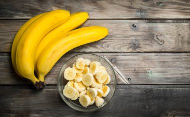 Cam bir kapta taze muz ve muz dilimleri. Ahşap bir arka plan üzerinde.