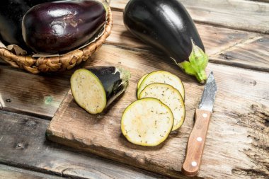 Pieces of eggplant on a cutting Board with a knife. On wooden background clipart