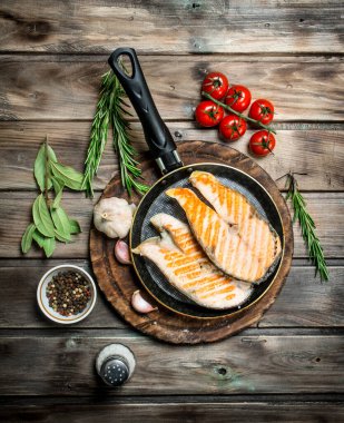 Baharat ve otlar ile bir tavada kızarmış som balığı. Ahşap bir arka plan üzerinde.
