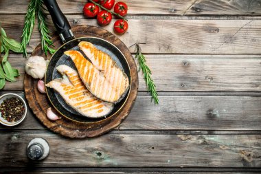 Baharat ve otlar ile bir tavada kızarmış som balığı. Ahşap bir arka plan üzerinde.