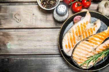 Baharat ve otlar ile bir tavada kızarmış som balığı. Ahşap bir arka plan üzerinde.
