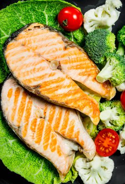 Somon ızgara biftek domates ve brokoli bir plaka ile. Rustik siyah arka plan üzerine.