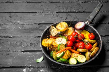 Otlar ve baharatlar ile bir tavada ızgara sebze. Siyah bir rustik arka planda.