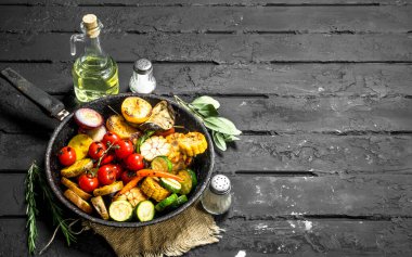 Otlar ve baharatlar ile bir tavada ızgara sebze. Siyah bir rustik arka planda.