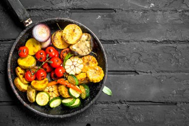 Otlar ve baharatlar ile bir tavada ızgara sebze. Siyah bir rustik arka planda.