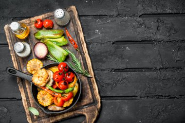 Bir tavada ahşap bir gemide baharat ile çeşitli ızgara sebze. Siyah bir rustik arka planda.