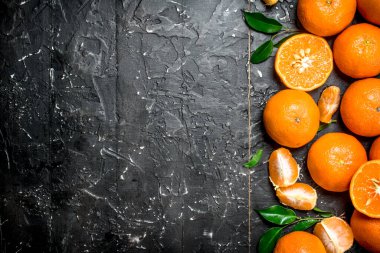 Whole and pieces of mandarins with leaves. On black rustic background