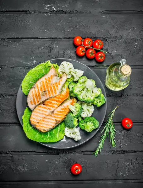 stock image Grilled salmon steaks with tomatoes and broccoli in a plate. On black rustic background.