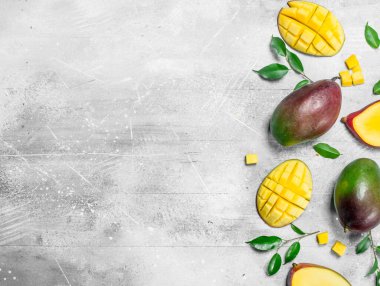 Bütün ve yaprakları ile olgun mango parçaları. Rustik arka plan üzerinde