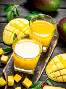 Mango suyu ve kesme tahtası üzerinde taze mango dilimleri. Ahşap arka plan üzerinde