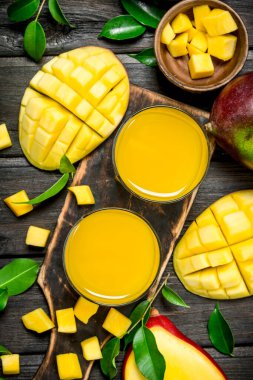 Mango suyu ve kesme tahtası üzerinde taze mango dilimleri. Ahşap arka plan üzerinde