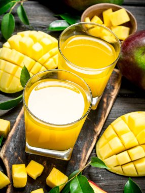 Mango suyu ve kesme tahtası üzerinde taze mango dilimleri. Ahşap arka plan üzerinde