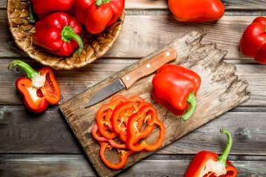 Bir bıçak ve bir sepet içinde olgun biber ile bir kesme tahtası üzerinde tatlı biber dilimlenmiş. Ahşap arka plan üzerinde