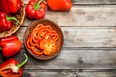 Bir kasede tatlı biber parçaları ve bir sepette bir bütün biber. Ahşap arka planda