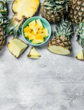 Yeşillikleri ile taze ananas ve kase dilimlenmiş ananas parçaları. Rustik arka plan üzerinde