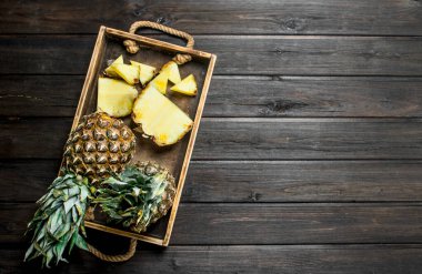 Whole and slices of ripe pineapple on a tray. On wooden background