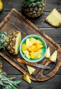 Bir kase ve bir bıçak ile kesme tahtası üzerinde bir ananas kesme. Ahşap arka plan üzerinde